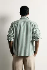 Camisa relaxed fit confeccionada en tejido de algodón, con diseño de rayas verticales en tonos azul y blanco, cuello con botones y manga larga.