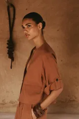 Chaqueta corta de escote en pico con cierre frontal de un botón. Presenta mangas cortas con detalle de vuelta, trabilla y botón, además de falsos bolsillos delanteros con solapa.