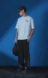 Remera blanca de corte oversize con cuello redondo y manga corta. Presenta una estampa gráfica en la espalda con diseño de palomas, flores y texto en español.