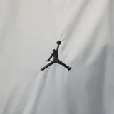 Campera rompevientos con capucha Nike Jordan, diseño color block en tonos gris claro, gris oscuro y negro. Presenta cierre frontal completo, bolsillos laterales y logo Jumpman bordado en el pecho.