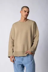 Sweater oversize de tejido de algodón color beige, con cuello redondo, puños y ruedo acanalados con detalles de desgaste. Presenta un diseño minimalista con etiqueta distintiva en el puño.