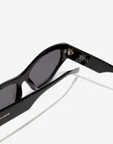 Lentes de sol Hawkers x Tini modelo Code, con armazón de acetato negro y diseño cat-eye. Presentan cristales oscuros y detalles de marca grabados en las patillas.