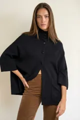 Cardigan negro de corte oversize, con cuello alto, cierre frontal de botones y mangas tres cuartos. Presenta un diseño holgado con bolsillos frontales y una caída fluida.