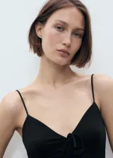 Vestido midi negro con tirantes finos, escote en V y detalle de lazo en el centro del busto. Diseño recto sin mangas y sin cierre.