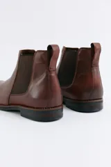 Bota tipo Chelsea de cuero negro con paneles elásticos laterales, suela de goma con detalle de vira en contraste y tirador trasero.