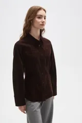 Camisa de pana color marrón, con cuello camisero, cierre frontal de botones y bolsillos en el pecho. Presenta un corte entallado y mangas largas.