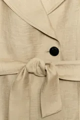 Chaleco de cuello solapa y manga sisa, color beige, con cierre frontal de un botón y cinturón ajustable del mismo tejido.