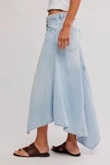 Falda larga de denim, de tiro medio y línea A, con abertura frontal, paneles con costuras y ruedo deshilachado en punta.