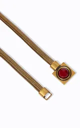 Cinturón fino y flexible de metal con acabado dorado, caracterizado por su diseño elástico y un detalle central cuadrado con una piedra roja. Su estructura permite un ajuste cómodo y versátil para realzar la cintura.