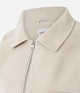 Campera bomber oversized de poliuretano con acabado efecto gamuza en color beige. Presenta cuello camisero, cierre frontal, mangas largas con puños abotonados y ruedo elástico.