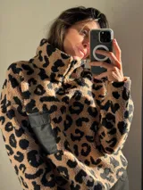 Buzo de corderito color beige con estampado animal print de leopardo en negro. Tiene cuello alto con cierre de cremallera y bolsillo tipo parche en el pecho de tela lisa color negro.