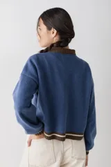 Cardigan de punto color crema con cuello redondo y cierre frontal de botones. Presenta detalles bordados de motivos celestiales y marinos, con terminaciones en tejido acanalado a rayas azules en cuello, puños y ruedo.