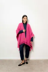 Ruana tejida color fucsia con flecos en el borde inferior.