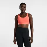 Top deportivo New Balance Essential Train Bra, color coral, de soporte medio, ideal para entrenamiento. Confeccionado en tejido de punto de poliéster con elasticidad y tecnología NB DRY de secado rápido. Cuenta con almohadillas extraíbles y banda inferior elástica.
