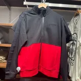 Campera deportiva Guess con cierre frontal, diseño color block en negro y rojo, cuello alto y mangas con detalle de cinta lateral con logo grabado.