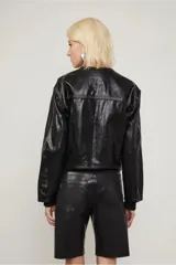 Campera negra efecto vinilo con terminación brillante y cuello redondo acanalado. Presenta bolsillos con solapa en el frente, costuras marcadas y cierre con broches a tono.