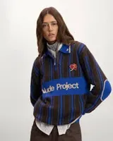 Sweater de punto Nude Project modelo Legend Football Knit Polo, con diseño a rayas en tonos azul y marrón. Cuenta con cuello polo con cierre frontal parcial, detalles bordados de una rosa y mariposas, y el nombre de la marca destacado en el pecho.