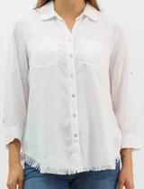 Camisa de tencel color blanco, con cuello camisero, cierre frontal de botones y dos bolsillos en el pecho. Presenta mangas largas con presilla para regular el largo y ruedo con detalle de flecos.