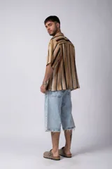 Camisa de manga corta con cuello cubano, confeccionada en tejido de punto con rayas verticales en tonos marrón, beige y negro. Presenta un corte holgado y botones frontales.