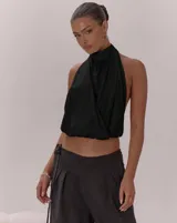 Top negro con escote halter y cuello alto. Presenta un diseño cruzado en el frente con pliegues, espalda descubierta con lazo regulable y bajo con terminación elástica.
