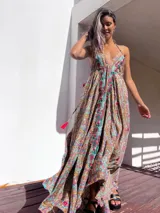 Vestido largo de estilo boho, con estampado tipo paisley en tonos tierra, turquesa y rosa. Presenta un escote profundo con tirantes finos y detalles de bordados florales en color rojo y verde a lo largo del frente.