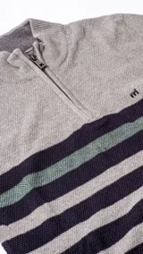 Buzo tejido de punto con medio cierre frontal, diseño a rayas horizontales en tonos gris, azul marino y verde. Presenta logo bordado en el pecho y cuello alto acanalado.