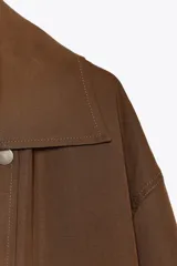 Trench color marrón confeccionado en mezcla de lyocell y lino. Cuello solapa y manga larga. Bolsillos con solapa en delantero. Cierre frontal con botones a presión.