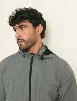 Campera impermeable gris con capucha, cierre frontal y bolsillos laterales con cremallera.