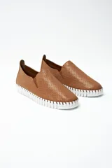 Zapatilla tipo slip-on de cuero color tostado, con textura perforada y suela de goma blanca con diseño dentado.