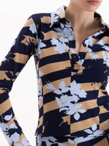 Remera de manga larga con cuello polo y cierre frontal parcial. Presenta un diseño estampado que combina rayas horizontales en tonos azul marino y tostado con un motivo floral en celeste.