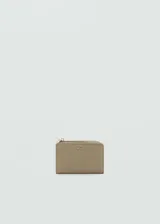 Billetera pequeña de mujer marca Mango, con acabado efecto saffiano en color beige. Cuenta con cierre de botón a presión, múltiples ranuras para tarjetas y un bolsillo exterior con cierre de cremallera. Incluye logo de la marca en relieve en la parte frontal.