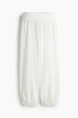Pantalón blanco de corte globo con cintura ancha fruncida y bajos elásticos. El tejido presenta una textura arrugada.