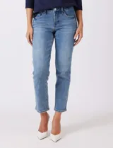 Jean azul de calce semi-ajustado, estilo Mom Slim, de tiro alto, relajado en la cadera y muslos, con pierna que se angosta levemente hacia el tobillo. Tiene pretina clásica con pasadores para cinturón, cierre frontal con cremallera y botón metálico, y bolsillos delanteros y traseros.