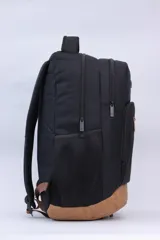 Mochila negra de tela con base y detalles en cuero sintético color camel. Presenta un bolsillo frontal vertical con cierre y un logo de montaña en relieve en la parte inferior. Tiene correas acolchadas y bolsillos laterales de malla.