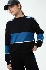 Buzo de punto con diseño de franjas horizontales en azul y blanco sobre fondo negro. Presenta cuello redondo, mangas caídas con puños elastizados y un corte holgado.
