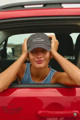 Gorra tipo baseball con efecto lavado vintage, color gris oscuro, con bordado en hilo blanco en la parte frontal que incluye el nombre de la marca y la frase La vuelta.