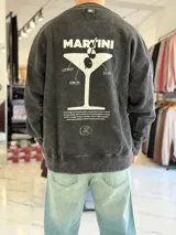 Buzo oversize color gris con efecto gastado (acid wash) y cuello redondo. Presenta un gran estampado en la espalda que ilustra una copa de martini con las inscripciones 'Martini', 'vermut', 'lemon' y 'olive', además de texto descriptivo y logo de la marca en la parte inferior.