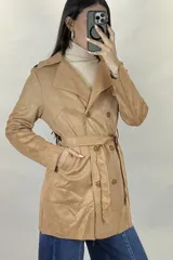 Trench de gamuza sintética color tostado, con diseño de doble botonadura, solapas clásicas y cinturón ajustable a la cintura. Cuenta con bolsillos laterales y mangas largas.