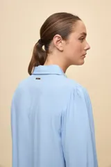 Camisa de calce relajado color celeste, con mangas 3/4, cuello clásico y cierre frontal con botones. Presenta detalles calados en el frente y en las mangas que aportan un acabado delicado al diseño.