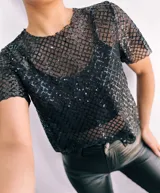 Remera negra de mangas cortas confeccionada en tejido de red con lentejuelas. Incluye top negro de breteles finos para usar debajo.