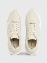 Zapatillas deportivas de mujer Calvin Klein, color beige claro, con cordones y suela gruesa blanca. Presentan una combinación de materiales que incluye piel natural y ecológica, con paneles de malla y detalles de monograma sutil en el lateral.