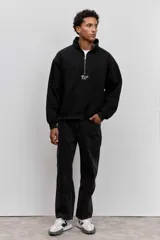 Buzo negro de cuello alto con cierre frontal parcial, manga larga y diseño holgado. Presenta un pequeño estampado gráfico en el centro del pecho.