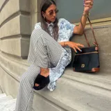 Bandolera negra de cuero sintético con detalles en marrón, cierre superior con cremallera y correa ajustable.