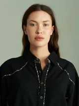 Camisa negra de algodón con mangas largas, cuello camisero y detalles de ribetes estampados a cuadros en los hombros, puños y aberturas de botones.