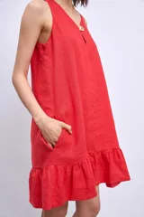 Vestido corto blanco sin mangas, con escote en V y detalle de broche dorado en el centro. La falda tiene un volado en el ruedo.