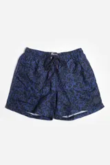 Short de baño celeste con estampado de hojas pequeñas en tonos verdes y blancos. Cuenta con cintura elástica con cordón ajustable, bolsillos laterales y un parche circular con logo en la parte inferior.
