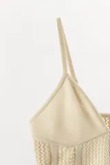 Top crop de punto color beige con escote en pico y tirantes finos ajustables. Presenta diseño con tejido calado y bajo de acabado asimétrico.