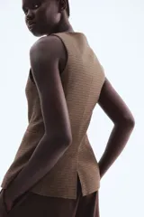 Chaleco largo sin mangas, con cuello redondo y cierre frontal de botones. Presenta un estampado de pata de gallo en tonos marrones y negros, bolsillos delanteros ribeteados y abertura en la parte trasera inferior.