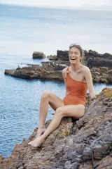 Malla enteriza color terracota con diseño asimétrico de un solo hombro, que presenta una argolla metálica decorativa en el tirante.