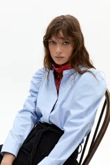 Camisa celeste de popelina 100% algodón, con cuello mao, hombros abullonados y mangas largas. Cierre frontal con botones de nácar.